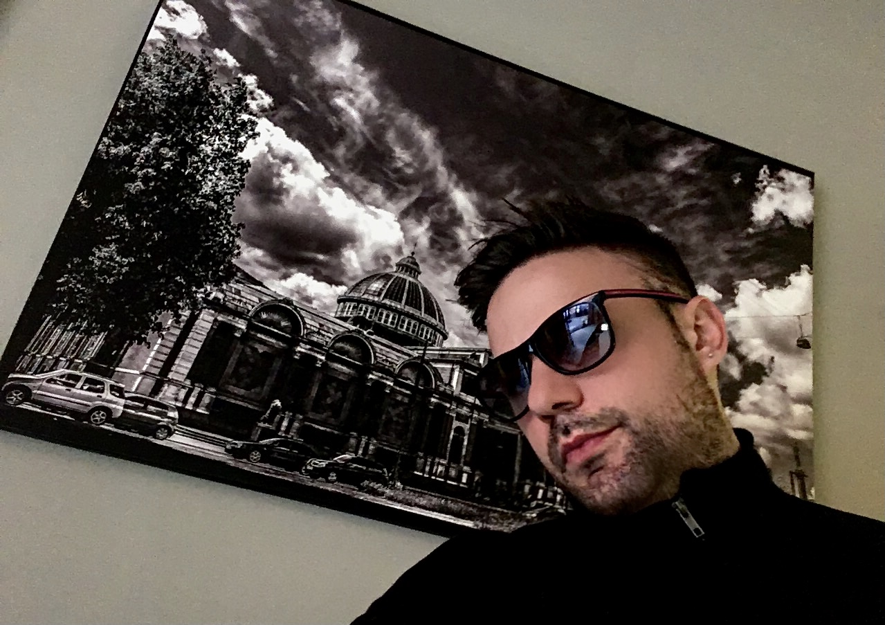 Gaetano Berardinelli — ritratto lifestyle con occhiali, opera d'arte sullo sfondo